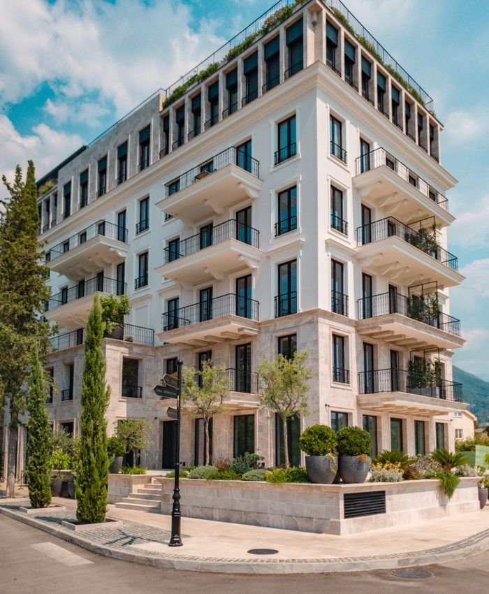 Elegant modern building with balconies and greenery in Tivat, Montenegro, under a clear blue sky.